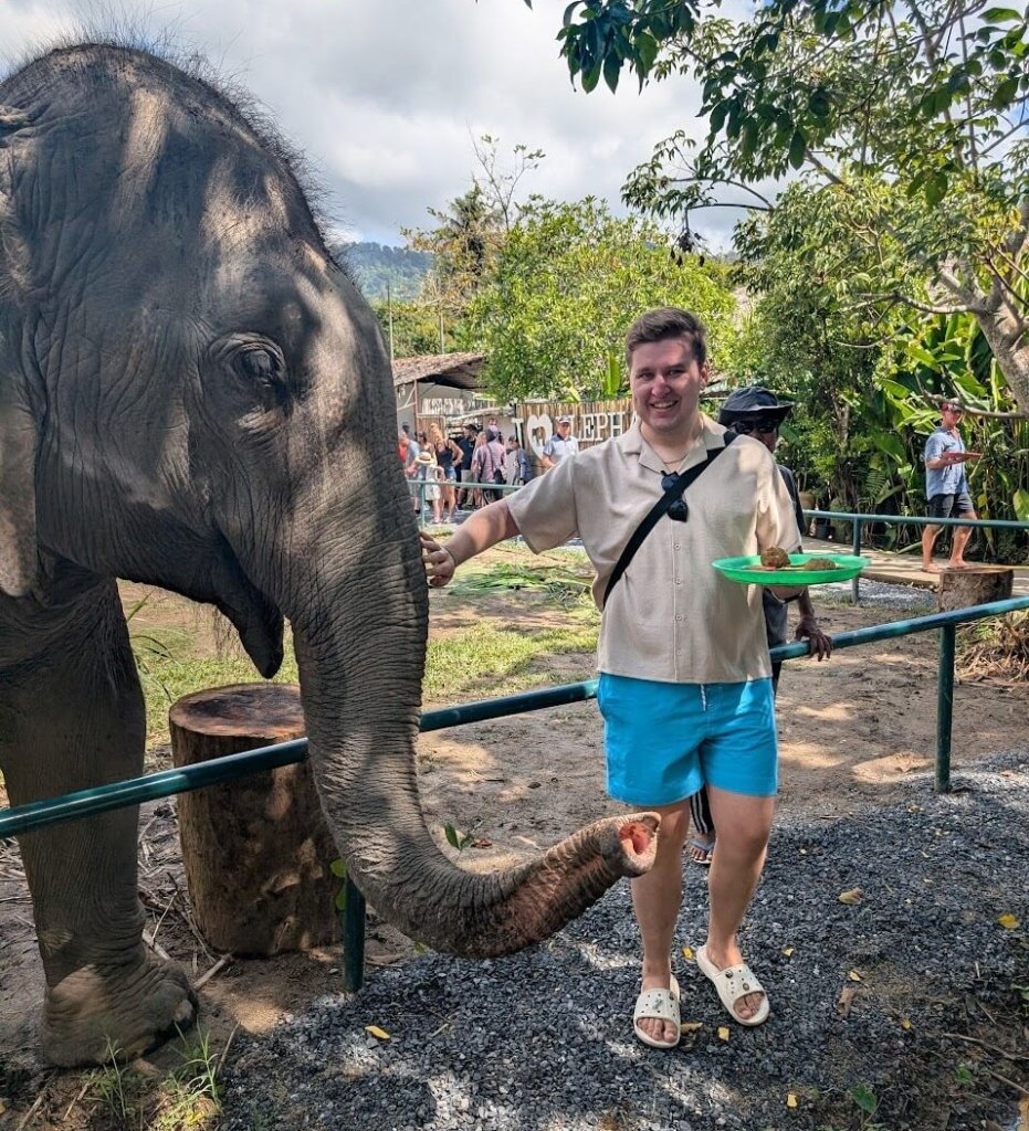 Tom Lejava, a solo travel blogger and creator of Tom Solo Travels in Thailand feeding an elephant in an elephant sanctuary